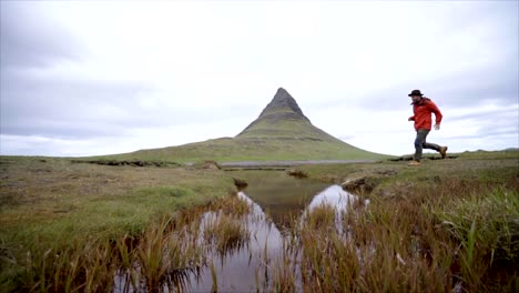 Hombre-joven-en-Islandia-saltando-sobre-Río-fiordo-en-la-famosa-montaña-de-Kirkjufell