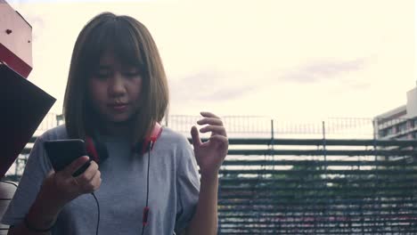 Beautiful-young-asian-woman-listening-to-music-on-a-smart-phone-in-the-city.-Young-asian-woman-relaxing-listening-to-music-on-the-street.