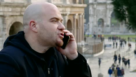 Angry-nervous-bald-man-talking-on-the-phone---colosseum-in-background