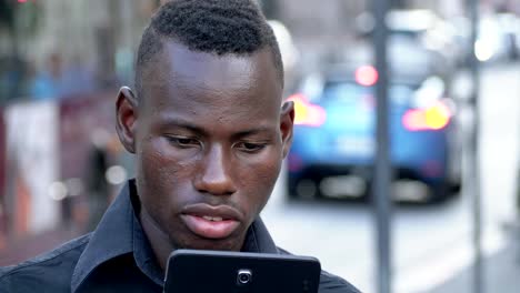 Smiling-american-african-young-man-typing-on-his-smartphone-outdoor