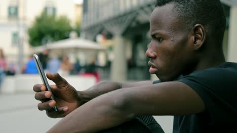 atractivo-negro-africano-joven-centrado-en-mecanografiar-en-el-smartphone-al-aire-libre