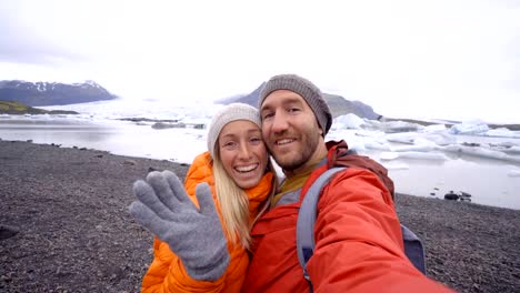 4-K-Video-der-jungen-Paare,-die-Spaß-unter-Selfie-durch-den-Gletschersee-Jökulsárlón-Lagune-in-Island.-Zwei-Personen-Reisen-Liebe-Romantik-Kommunikationskonzept-miteinander-teilen.-Frühling,-Kälte