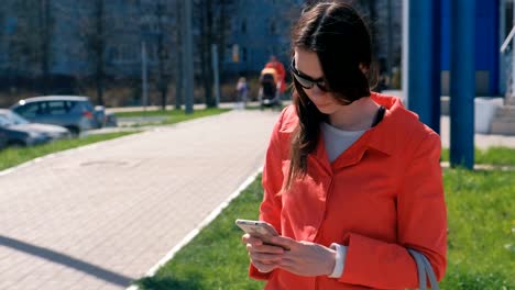 Mujer-joven-morena-en-gafas-de-sol-en-capa-roja-espera-a-alguien-y-comprueba-su-teléfono,-mensajes-de-texto.