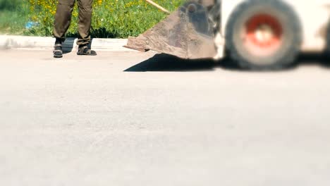 Limpieza-de-la-zona-urbana.-Hombre-recoge-la-suciedad-con-una-pala-y-todo-lo-arroja-en-el-cubo-de-la-excavadora.-Primer-plano-de-las-piernas.