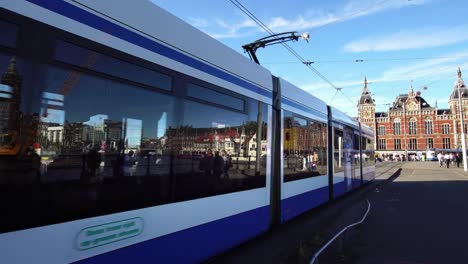 Tram-train-passes-Central-Railway-Station-in-downtown-Amsterdam,-Europe.