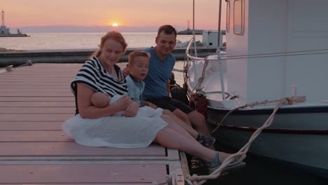 Parents-with-elder-son-and-baby-sitting-on-the-pier-at-sunset