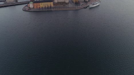 Aerial-view-of-Stockholm-city-center.-Drone-shot-flying-over-water-and-camera-tilt-up-on-Riddarholmen-island-and-Old-Town-buildings-and-towers.-Capital-city-of-Sweden