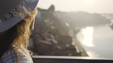 Lady-in-hat-drinking-from-cup-standing-on-bridge