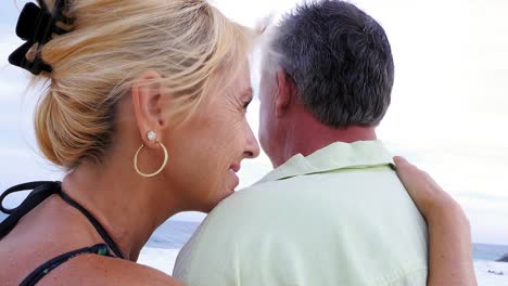 Close-up-of-an-older-couple-at-the-beach-with-their-arms-around-each-other-and-being-affectionate