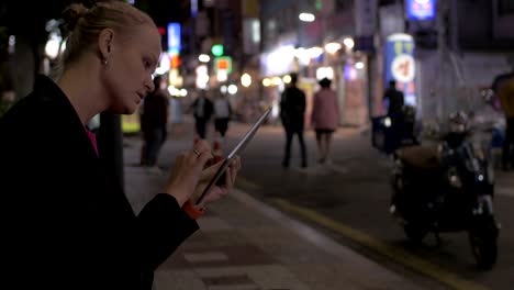 Woman-working-with-pad-in-night-Seoul-street,-South-Korea