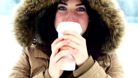 Smiling-woman-in-fur-jacket-having-coffee-during-snowfall