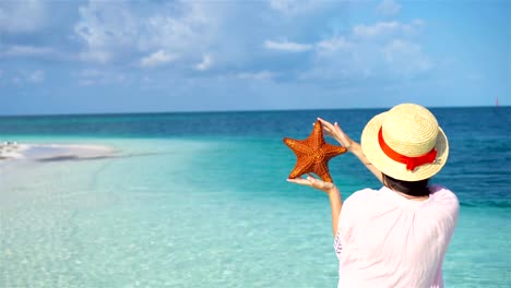 Junge-Frau-mit-Seestern-am-weißen-Strand-im-Naturschutzgebiet