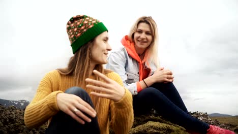 Two-happy-woman-sitting-on-the-lava-field-covered-moss-in-Iceland-and-talking.-Tourists-friends-resting-after-hiking