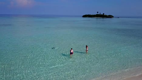 v03811-Aerial-flying-drone-view-of-Maldives-white-sandy-beach-on-sunny-tropical-paradise-island-with-aqua-blue-sky-sea-water-ocean-4k-2-people-young-couple-man-woman-playing-ball-fun-together