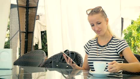 Young-girl-is-sitting-in-a-summer-cafe,-drinking-delicious-coffee-and-writing-a-message-on-the-phone.