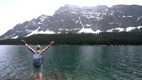 Young-woman-arms-outstretched-by-mountain-lake