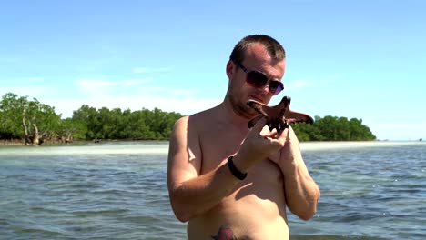 A-man-stands-at-sea-and-looks-at-a-starfish