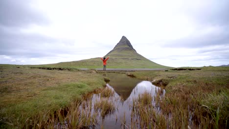 4K---Young-man-in-Iceland-arms-outstretched-for-freedom-Springtime-overcast-sky-at-famous-Kirkjufell-mountain