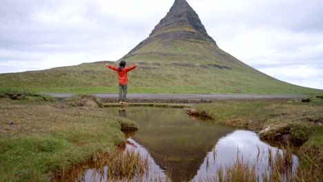 4K---Young-man-in-Iceland-arms-outstretched-for-freedom-Springtime-overcast-sky-at-famous-Kirkjufell-mountain