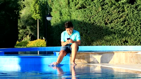 Muchacho-joven-usando-el-teléfono-inteligente-cerca-de-la-piscina