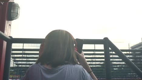 Schöne-junge-asiatische-Frau-anhören-von-Musik-auf-einem-Smartphone-in-der-Stadt.-Junge-asiatische-Frau,-entspannende-Musik-hören-auf-der-Straße.