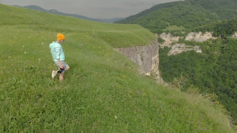 The-girl-photographer-in-glasses-and-a-hat-walks-with-her-dslr-camera-on-the-edge-of-the-plateau-near-the-precipice.-Aerial-view