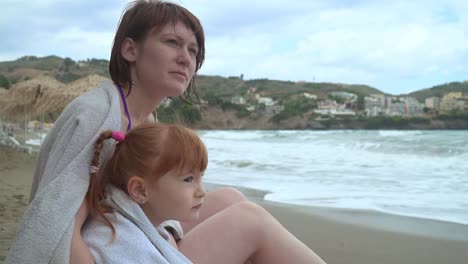 Mutter-und-Tochter-am-Strand-sitzen-und-schauen-auf-das-Meer