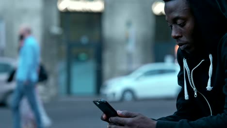 Schwarze-afrikanische-junger-Mann-sitzt-auf-der-Straße-Tippen-auf-smartphone