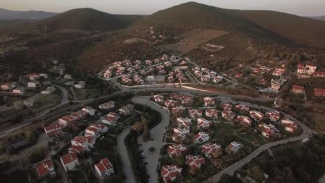 Aerial-scene-of-neighbourhood-and-green-hills-in-Trikorfo-Beach,-Greece