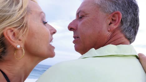 Close-up-of-an-older-couple-at-the-beach-with-their-arms-around-each-other-and-being-affectionate