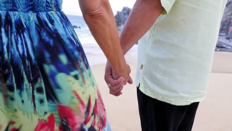 Close-up-of-an-older-couple-holding-hands-and-looking-out-at-the-ocean