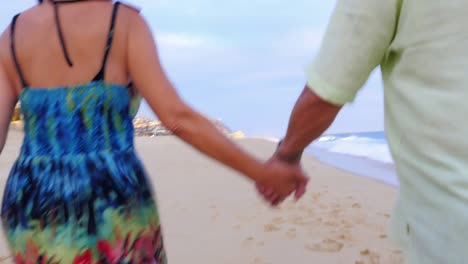 Close-up-of-an-older-couple-holding-hands-and-walking-down-the-beach