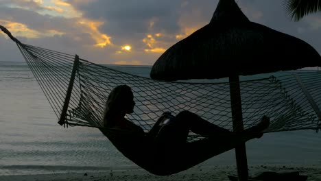 Mujer-relajante-en-hamaca-en-la-playa-y-toma-fotos-de-celular