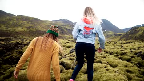 Two-tourists-woman-walking-through-the-lava-field-in-Iceland-covered-moss.-Girls-raises-hands,-feels-happy-and-freedom