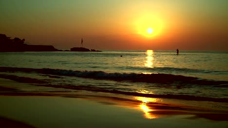 Silhouette-of-a-surfer,-swims-across-the-path-from-the-sun-to-the-sea-at-sunset.