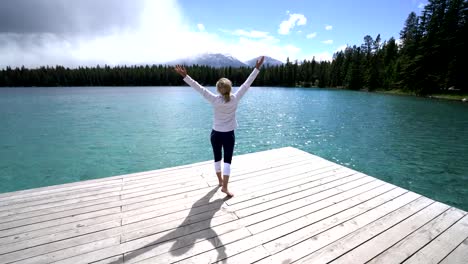 Young-woman-arms-outstretched-on-lake-pier,-Canada