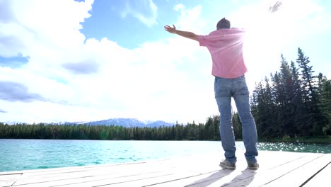 Young-man-arms-outstretched-on-lake-pier,-Canada