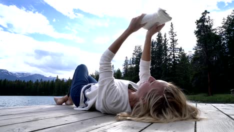 Mujer-joven-relajante-en-el-muelle-del-lago-con-el-libro,-Canadá