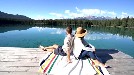 Young-couple-sitting-on-wooden-pier-above-magnificent-mountain-lake-admiring-nature