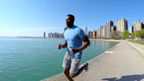 Ethnic-male-running-along-Chicago-shoreline-by-skyscrapers