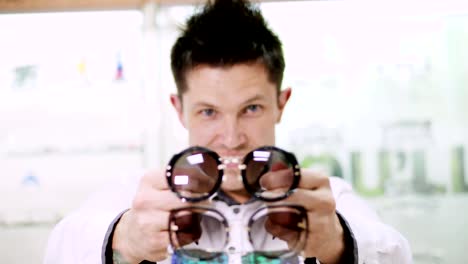 portrait-of-sexy-smiling-Handsome-man-staring-at-camera.-holding-lots-of-colorful-spectacles,-sunglasses,-at-the-same-time-in-his-hands,-in-front-of-his-face.-man-dressed-in-white-shirt