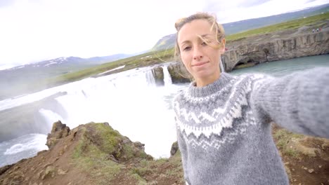 Cae-joven-mujer-tomando-selfie-retrato-con-magnífica-cascada-en-Islandia,-Godafoss.-Gente-viaje-exploración-concepto