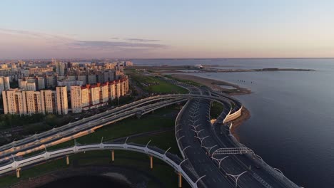 Cars-going-on-multi-level-road-junction-on-the-sea-shore-with-city-buildings-on-the-sunset