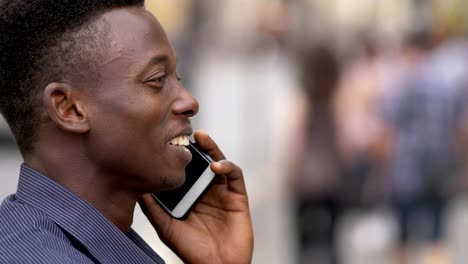 Smiling-young-american-african-man-talking-by-phone-in-the-street--profile