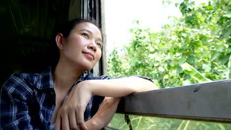 4K.-asian-woman-travel-by-train-looking-out-of-a-train-window-on-railway-train-start-at-Bangkok-go-to-Kanchanaburi-in-Thailand.-enjoy-transportation-by-vintage-train