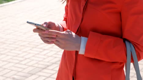 Nicht-erkennbare-Frau-im-roten-Mantel-wartet-auf-jemanden-und-überprüft-ihr-Handy-SMS.-Close-up-Hände.