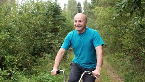 Senior-hombre-caucásico-en-camiseta-azul-disfrutando-de-sus-vacaciones-de-verano,-andar-en-bicicleta-al-aire-libre-entre-los-árboles.