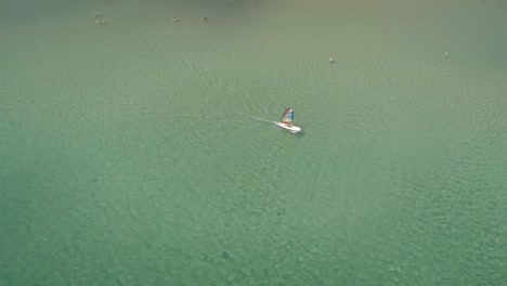 Aerial-view-of-man-windsurfing-on-a-beach-with-people-swimming-in-Greece.