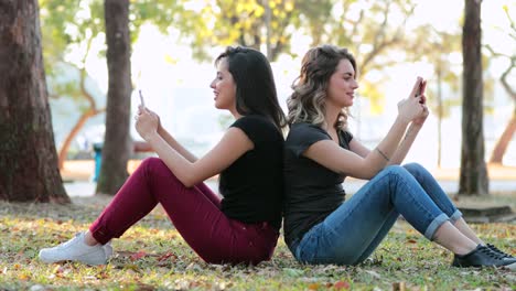 Freunden-zusammen-im-freien-Internet-Media-Inhalten-zusammen-teilen.-Freundinnen-sitzen-draußen-im-Park-mit-smartphones