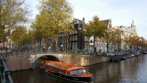 barco-de-paseo-naranja-pasando-por-debajo-de-un-puente-canal-en-amsterdam